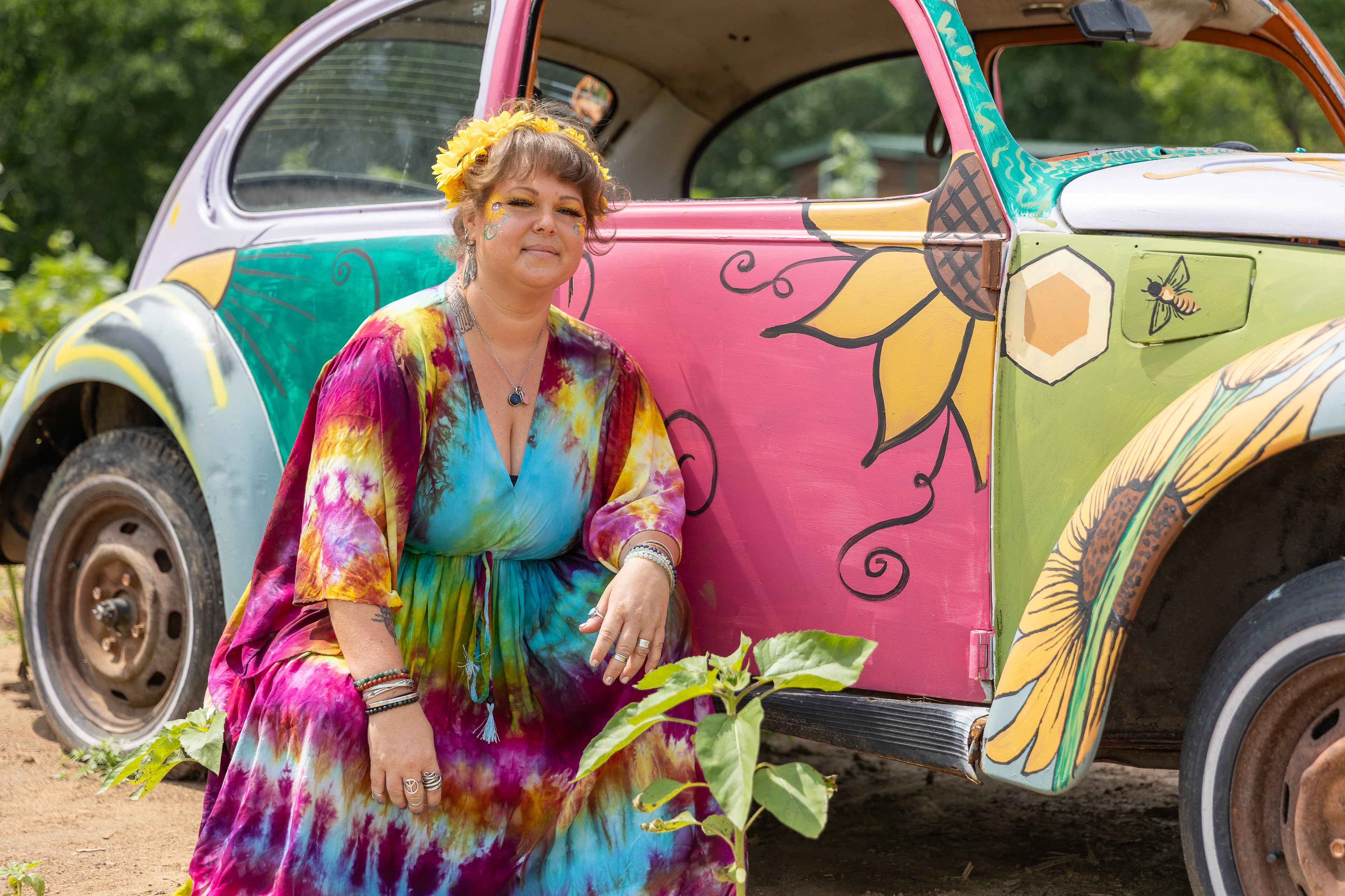 Woman in a tie-dye dress standing next to a colorful vintage car.